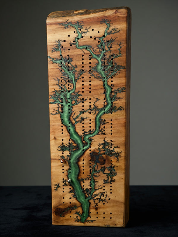 A rectangular wooden board with a natural grain pattern, featuring a green tree-like inlay and rows of small black peg holes, photographed against a dark gray background.
